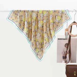 Detail of khakhi silk scarf featuring daisy floral patterns and blue contrast hem