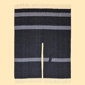 Detail of black knit shawl with grey stripes and fringe trim on a cream background