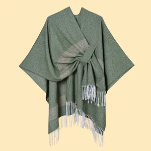 Detail of olive green knit shawl featuring grey stripes and thick white fringe tassels