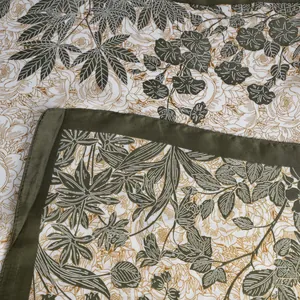 Detailed close-up of floral print satin scarf featuring green leaves and fine gold outlines