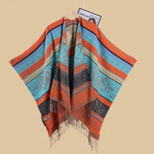 Ethnic jacquard knit poncho with bohemian patterns and fringe displayed on a wooden hanger
