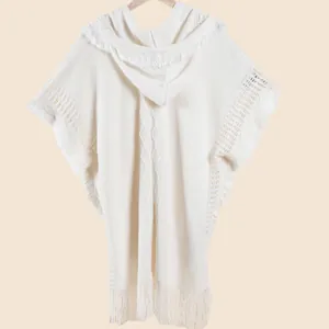 Close-up of white knit poncho featuring tassel fringe and diamond geometric textures