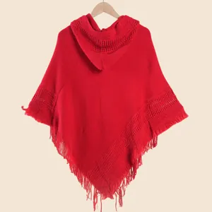 Détail d'un poncho à capuche en maille rouge avec motifs texturés et finitions franges
