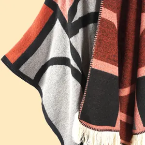Détails de la maille et des franges beiges du poncho géométrique aux motifs rouge brique