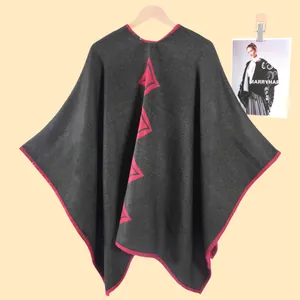 Dettaglio di un poncho in maglia con motivi geometrici rossi e bordi arrotolati