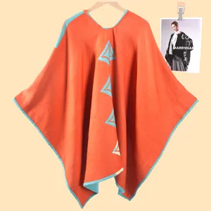 Dettaglio di un morbido poncho in maglia con motivi geometrici arancioni e blu e scollo a V