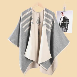 Dettaglio del poncho in maglia grigio e beige con motivi geometrici e texture a righe