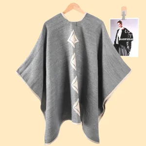 Dettaglio del poncho grigio in maglia con motivi a rombi bianchi e bordi rifiniti