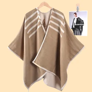 Dettaglio del poncho in maglia con strisce diagonali e bordo rifinito su gruccia in legno