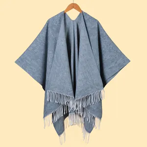 Detail of grey-blue knitted shawl with thick white fringe tassels and textured twill fabric