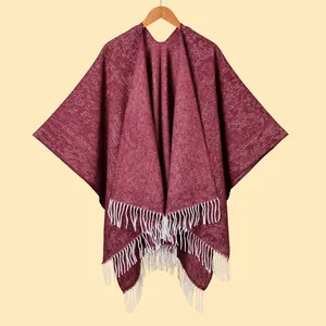 Detail of burgundy knit shawl featuring thick texture and contrasting white fringe tassels