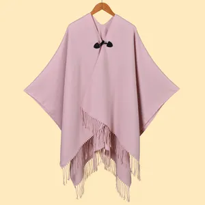 Details eines hellrosa Strickponchos mit schwarzer Lederschnalle und langen Fransenquasten