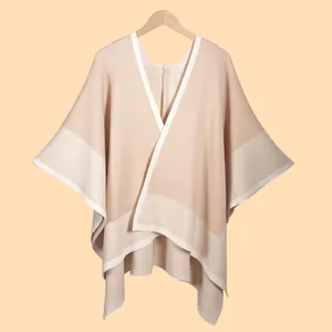 Detailed knit texture of a beige V-neck cape with contrast white hem borders