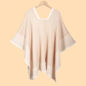 Detailed view of beige knit poncho with contrasting white trim and textured fabric