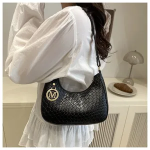 Close-up detail of a black woven textured shoulder bag with a gold letter M pendant