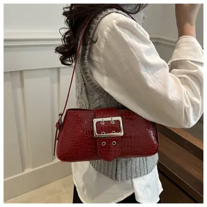 Detail view of burgundy croc-effect shoulder bag with a silver buckle worn by a model