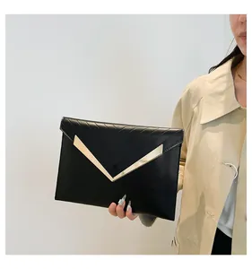 Detail of black V-quilted envelope clutch featuring luxury gold metal hardware and texture