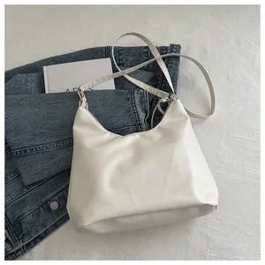 Borsa tote minimalista in ecopelle bianca su tessuto bianco accanto a una giacca di jeans