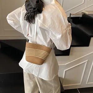 Sac seau en paille rayé avec bandoulière marron porté par un mannequin en intérieur