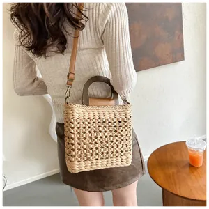 Detail of woven straw bag showing the dark wood handles and leather shoulder strap