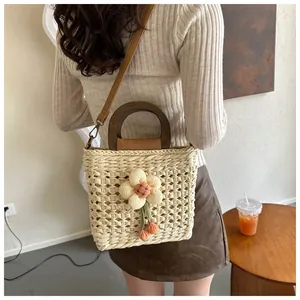 Detail of hand-woven straw bag with wooden handles and delicate 3D floral accent