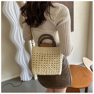 Detail of hand-woven straw bag featuring wooden ring handles and a brown leather strap