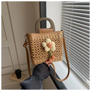 Close-up of a woven straw handbag with a 3D floral accent and wooden handles