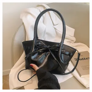 Detail shot of a black glossy bucket bag featuring a large bow and elegant top handle
