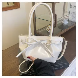 White patent leather bucket bag with large bow detail on a black art book display