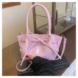 Close-up of pink glossy leather bucket bag with decorative ribbon and gold hardware
