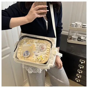 Detail of white canvas Ita bag featuring transparent window with lace and anime pins