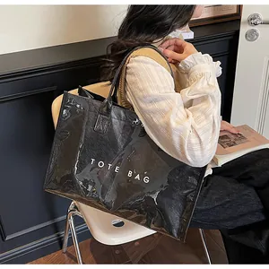 Close-up of a large black glossy tote bag with white TOTE BAG text carried by a model