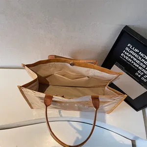 Minimalist clear PVC tote bag with brown leather trim and large interior zip pocket