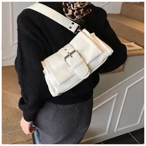 Detailed view of beige leather crossbody bag with broad strap and silver buckle accent
