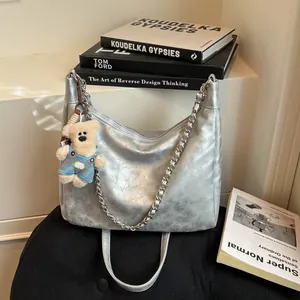 Sac hobo argenté avec bandoulière chaîne et breloque ours sur tabouret noir