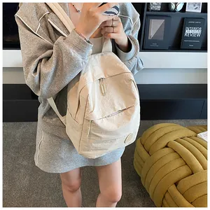 Dettaglio dello zaino in nylon beige minimalista con trama stropicciata e logo
