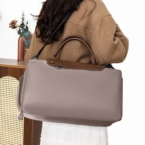 Large taupe travel tote with brown leather handles worn by a model in a cozy interior