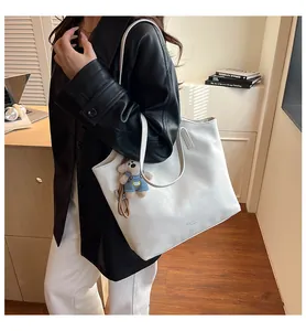 Detail of white faux leather tote bag with long straps and cute bear charm pendant