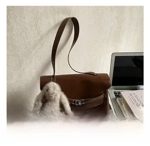 Detail of a brown leather shoulder bag with a metal buckle and a plush rabbit charm