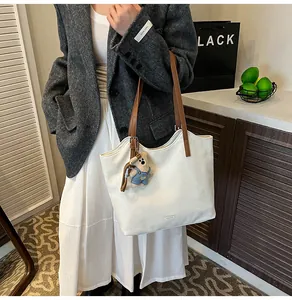 Detailed view of white leather tote bag with brown straps and cute bear pendant