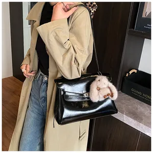 Detail of black patent leather shoulder bag with silver buckle and plush rabbit charm