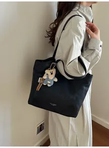 Detail view of large black matte leather tote bag featuring a cute plush bear charm