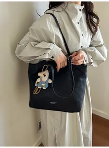Detail of a large black matte leather tote bag featuring a cute plush bear charm