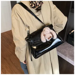 Detail of glossy black leather shoulder bag with a cute pink plush bunny charm accessory