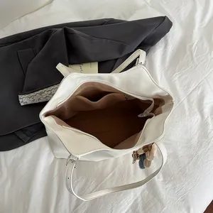 White minimalist tote bag with adjustable handles and plush bear charm for daily use