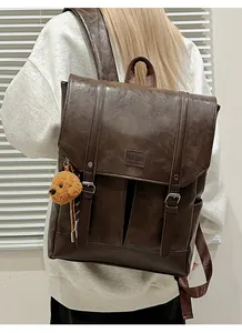 Detail of vintage brown leather backpack with silver buckles and a cute bear keychain charm