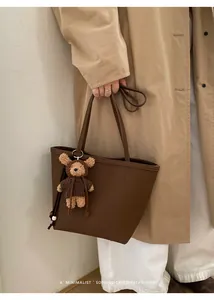 Detail shot of a retro brown tote bag featuring a cute teddy bear charm on the shoulder strap