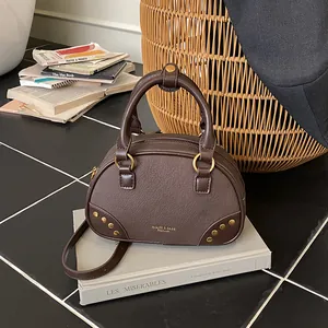 Retro dark brown faux leather crossbody bag with gold rivets on stack of books