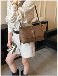 Détail du sac bandoulière en cuir marron avec boucle argentée porté par le mannequin
