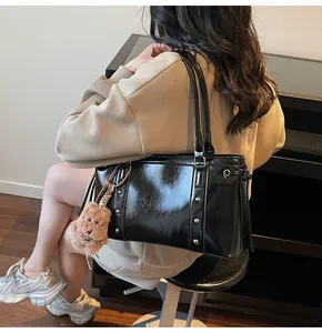 Detail view of glossy black faux leather tote with silver rivets and bear charm ornament